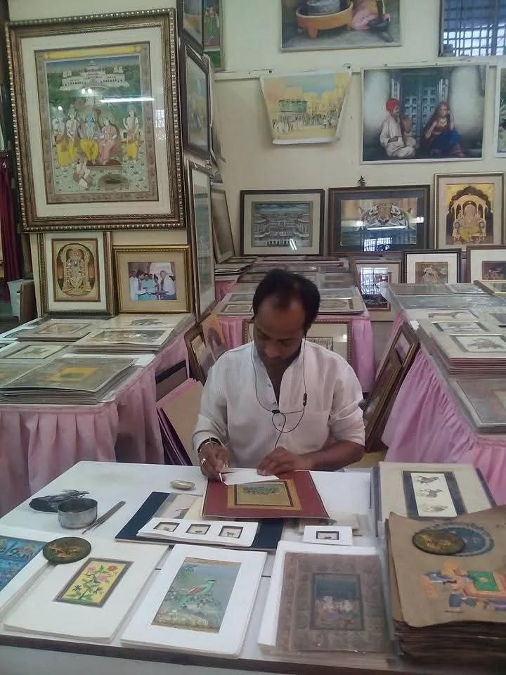 A painter at work at a table of miniatures, among framed paintings