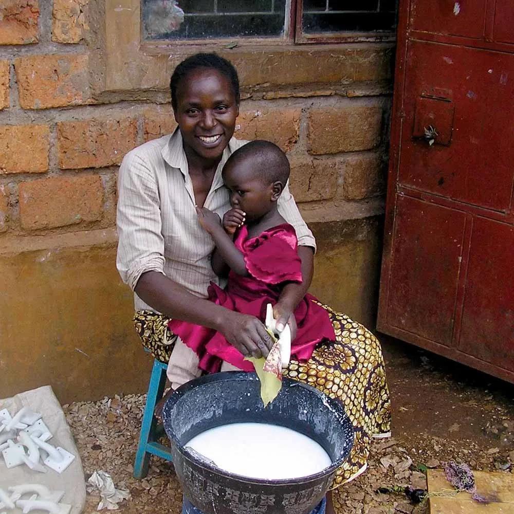 A smiling woman polishing a soapstone piece with her young child on her lap