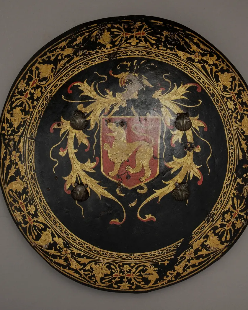 A black lacquered ceremonial shield with gilded scrollwork and a central coat of arms
