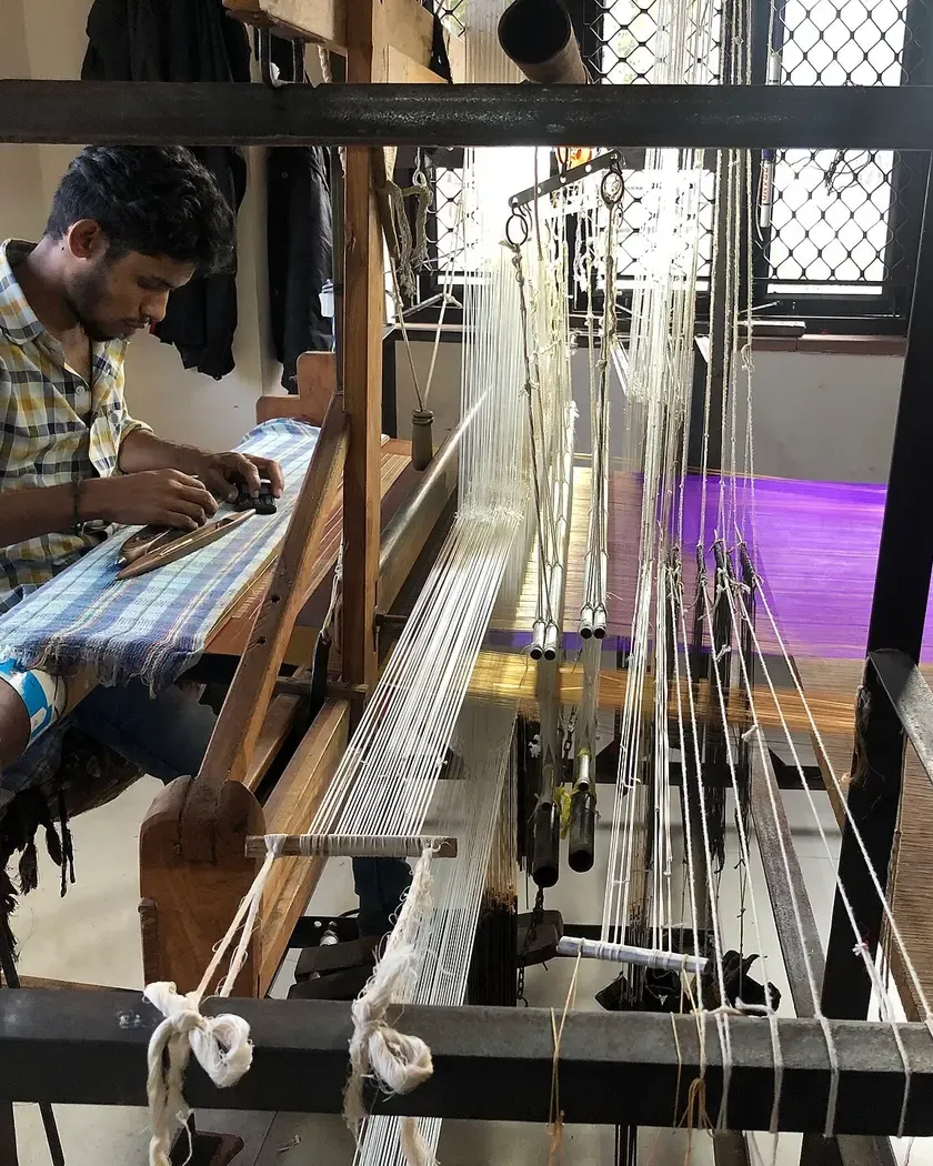 A weaver at a handloom passing the shuttle through a blue warp